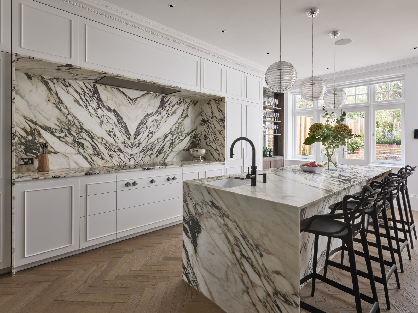 Kitchen with a veined marble island and splashback, painted cabinetry and herringbone oak flooring