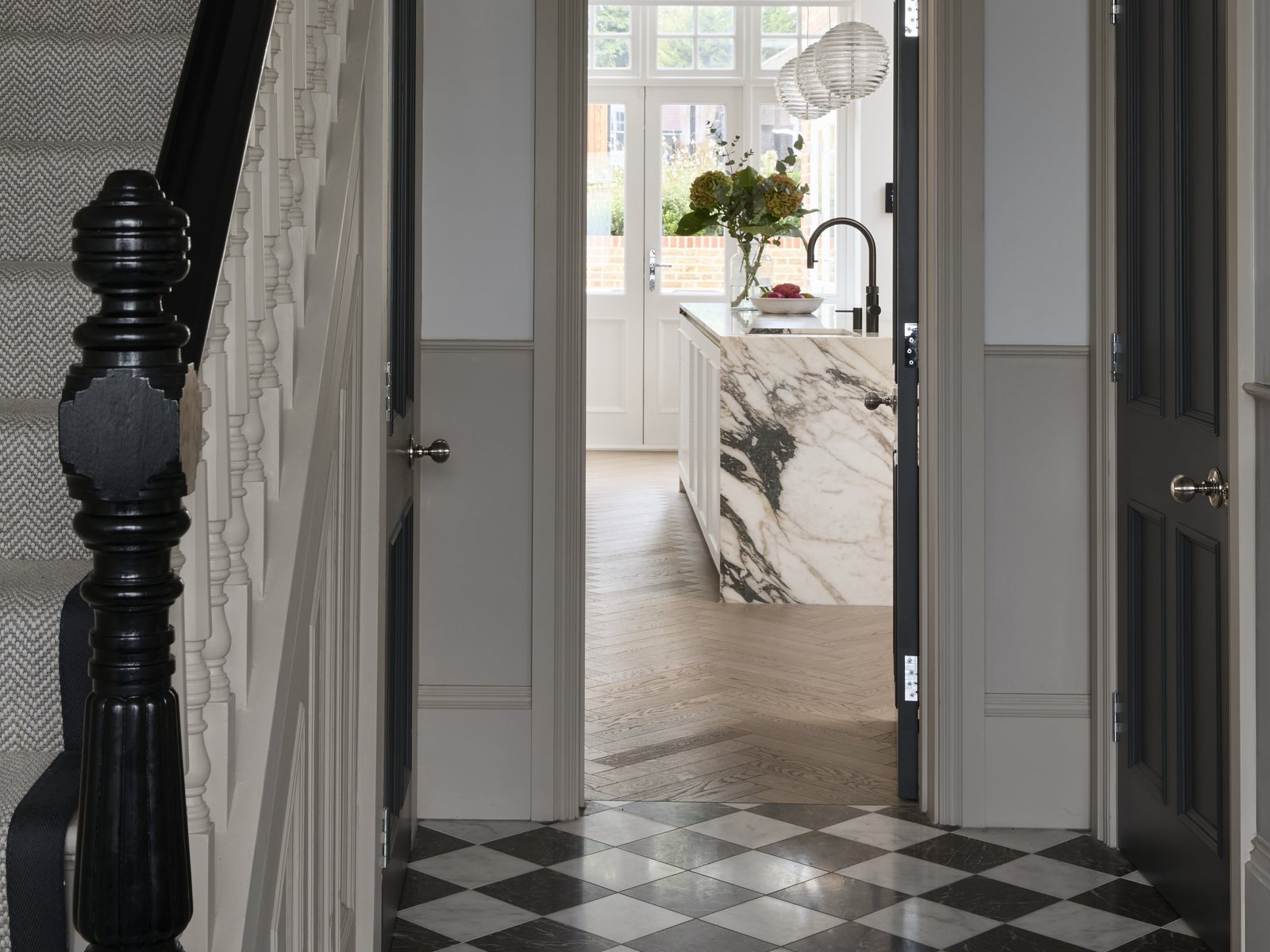 Entrance hall with a chequerboard stone floor and painted staircase, looking through to the kitchen