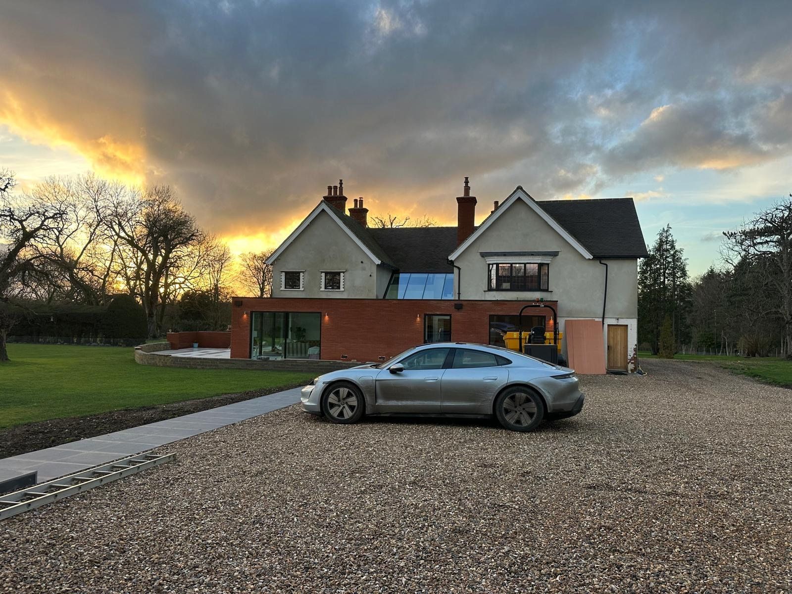 House at dusk with a new full-width single-storey brick extension, sliding glazed doors and a gravel drive