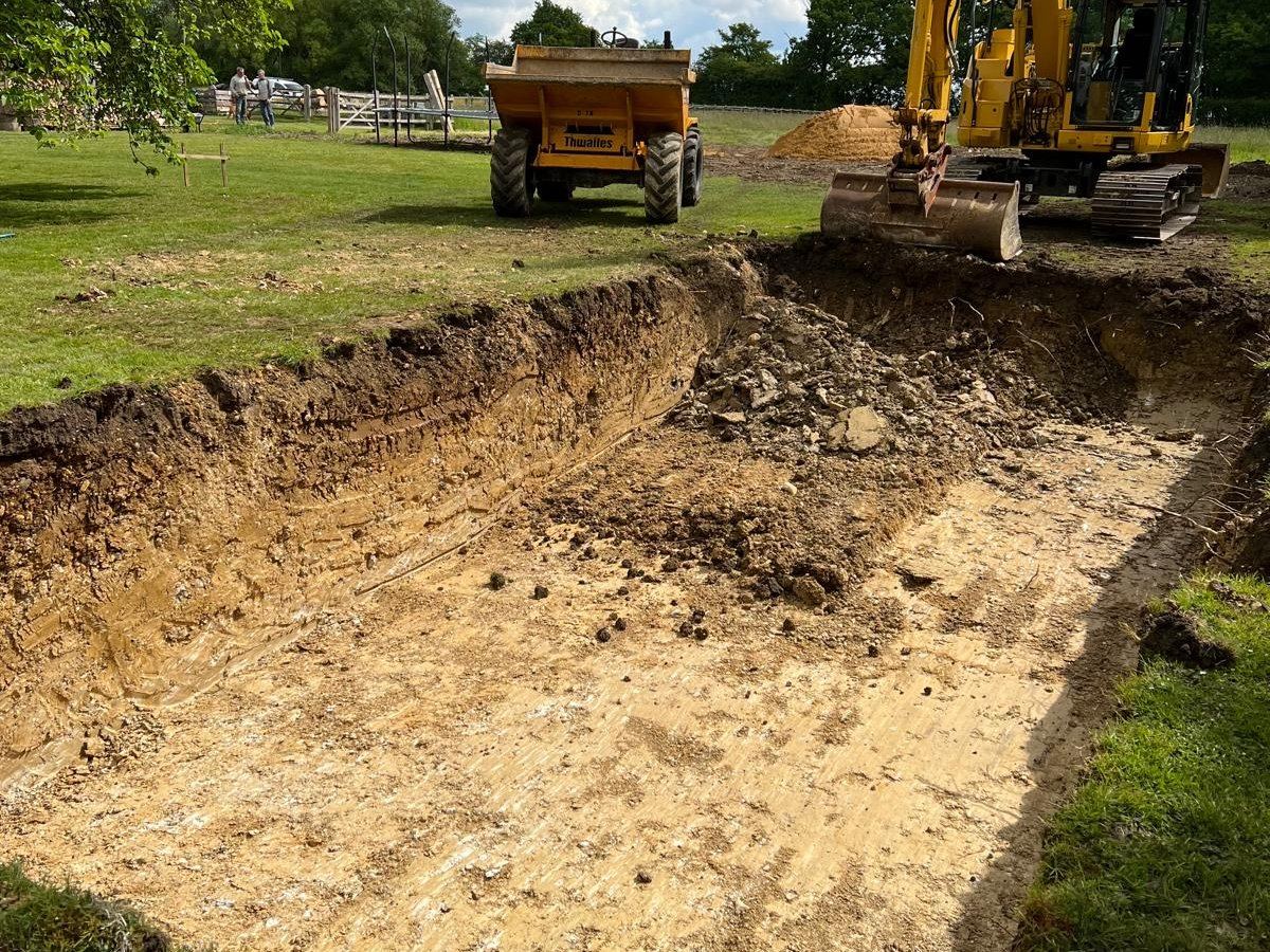 Swimming pool under construction: the excavation dug out, with an excavator and tipper alongside